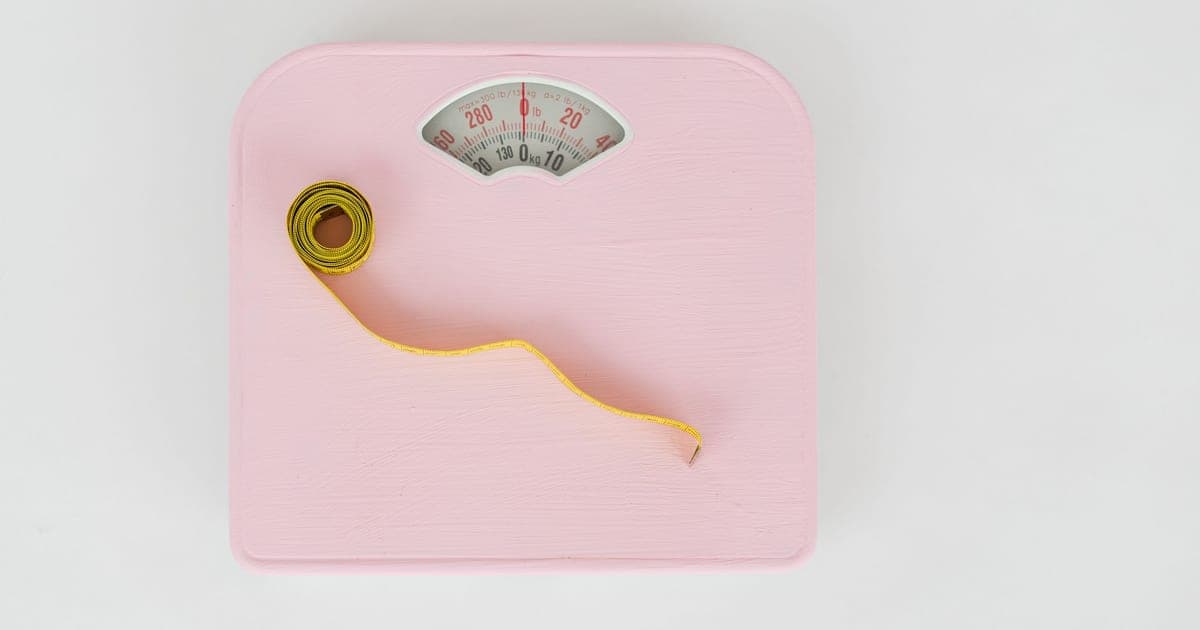 Bathroom scale beside a tape measure and a kitchen food scale, illustrating why the scale cannot show body recomposition