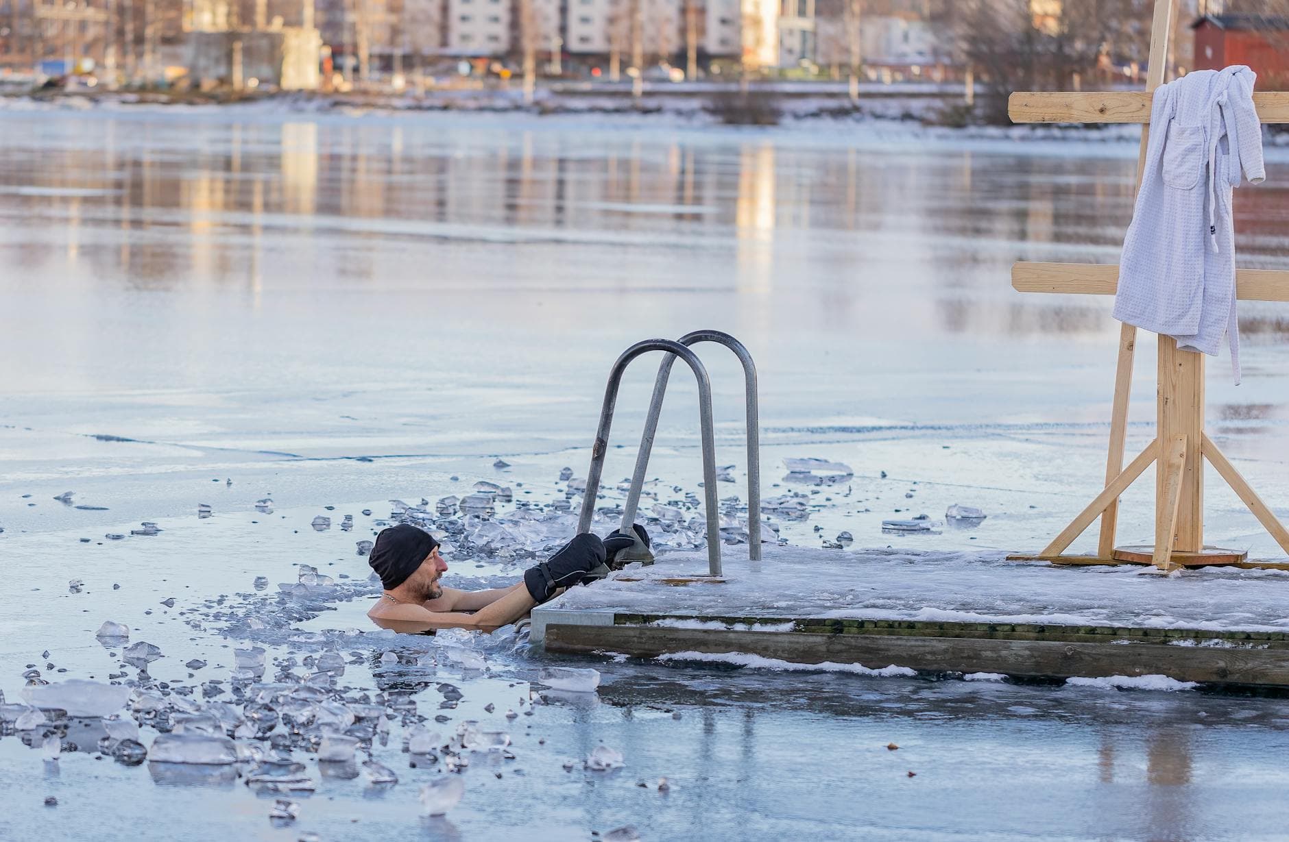 Man getting into icy cold water near a wooden dock in a winter landscape