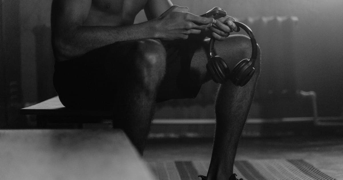 Athlete sitting on a gym bench between sets checking readiness on a phone, deciding whether to push through or deload