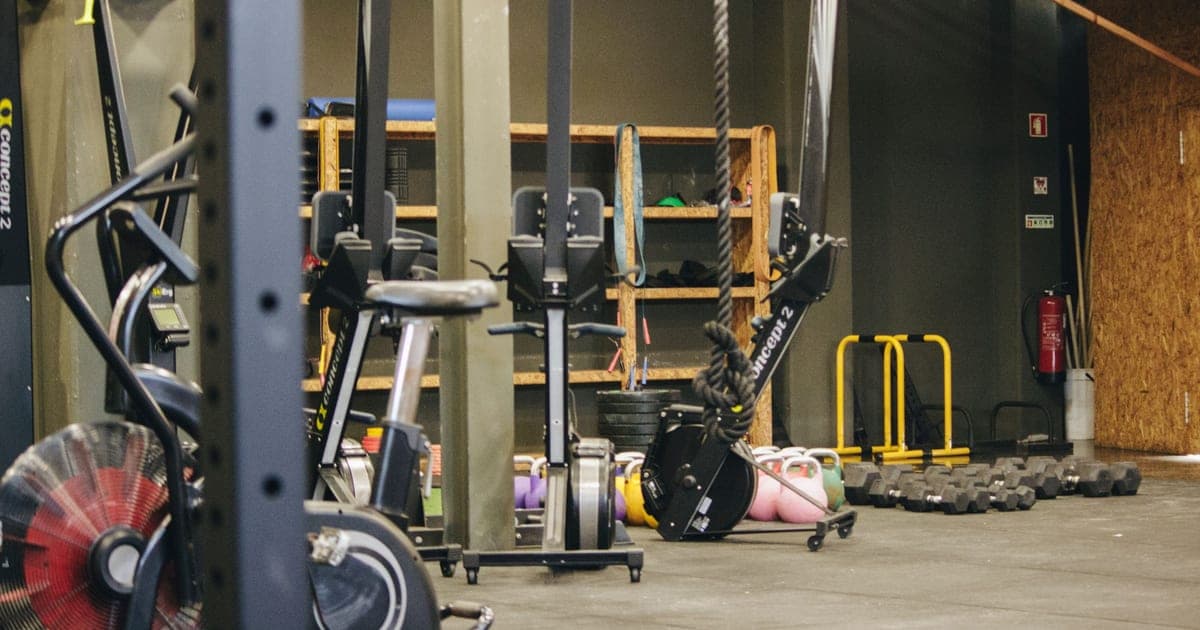 Person on a stationary bike in a gym with weight racks visible in the background, illustrating concurrent cardio and strength training