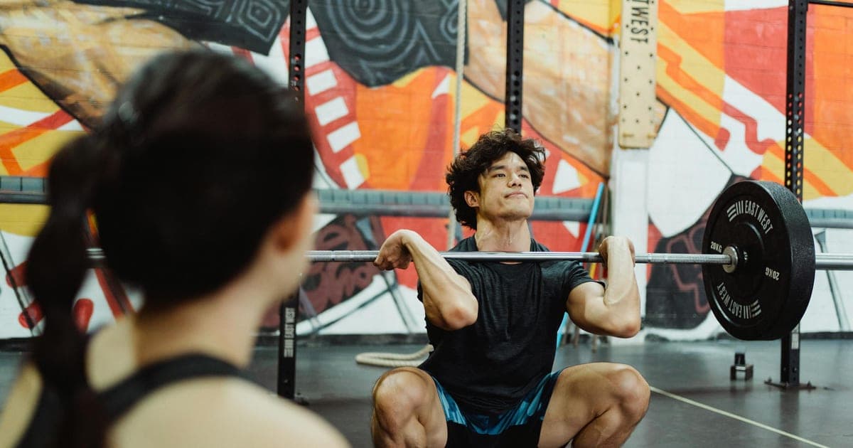 Two people with visibly different body types training side by side in a gym, performing the same barbell exercise