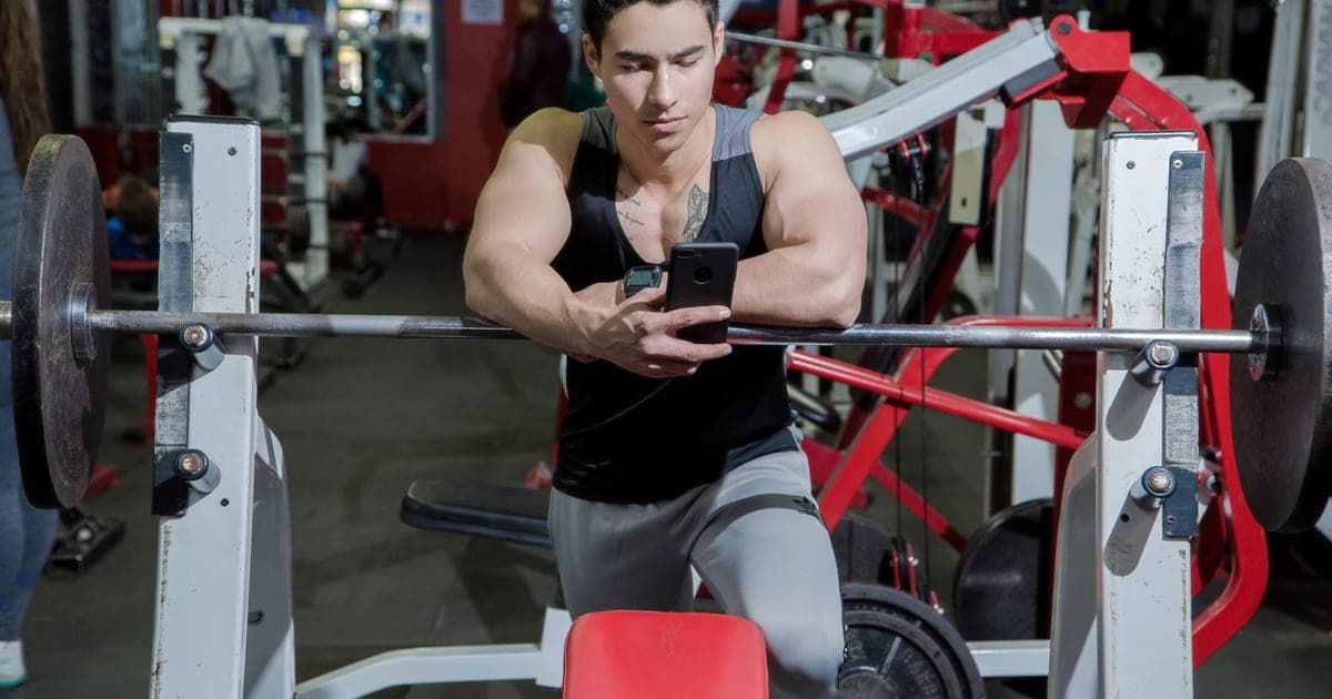 Lifter at a bench press station between sets, looking at his phone, with nobody else paying attention