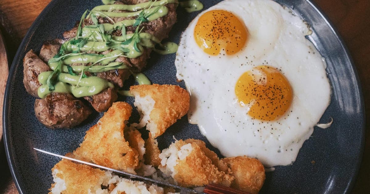 Large protein-rich meal with steak and eggs on a plate, illustrating higher protein per meal for muscle building