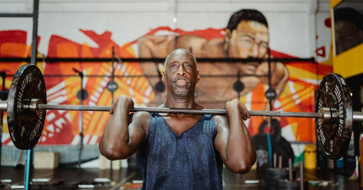 Middle-aged professional performing a barbell squat in a gym, illustrating resistance training as a cardiovascular health investment