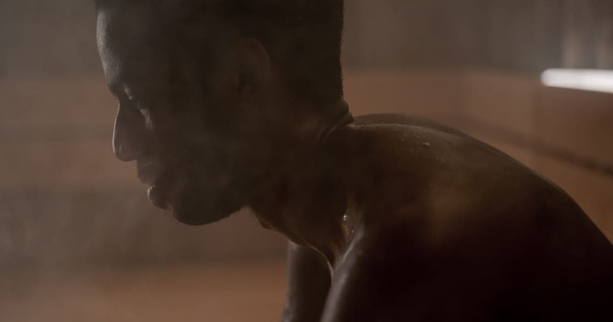 Man in gym clothes sitting on a wooden sauna bench with a towel, about to head out to train