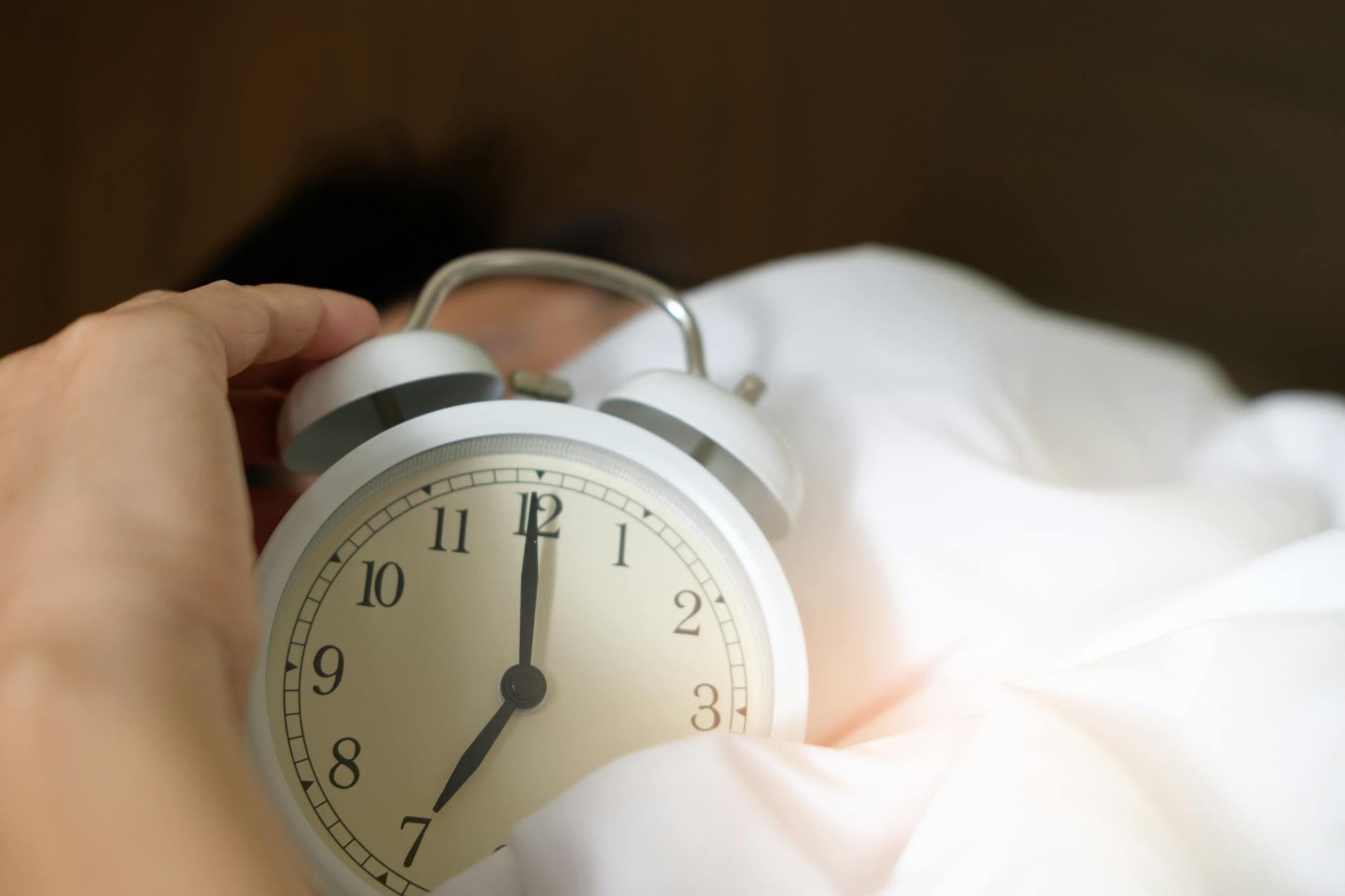 Person sitting on the edge of a bed checking their phone at 4am with gym clothes laid out beside them