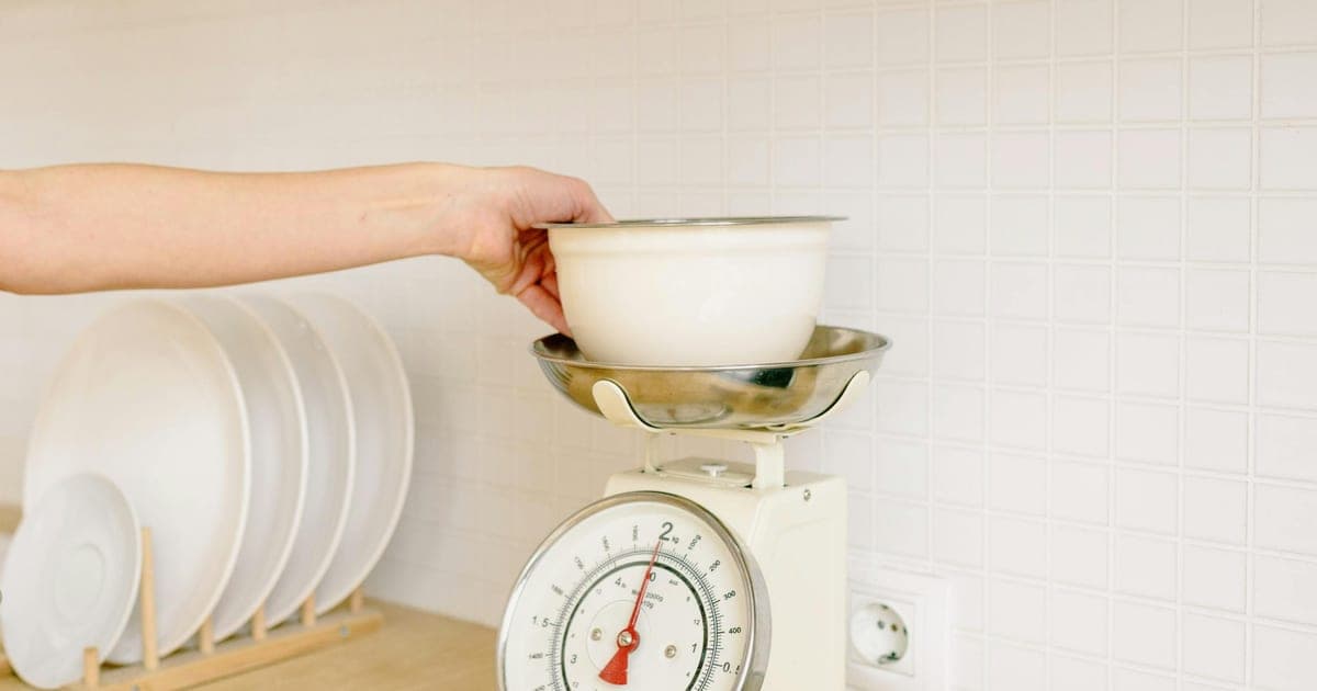 Person weighing food on a kitchen scale next to a training log, illustrating a moderate calorie deficit and muscle preservation